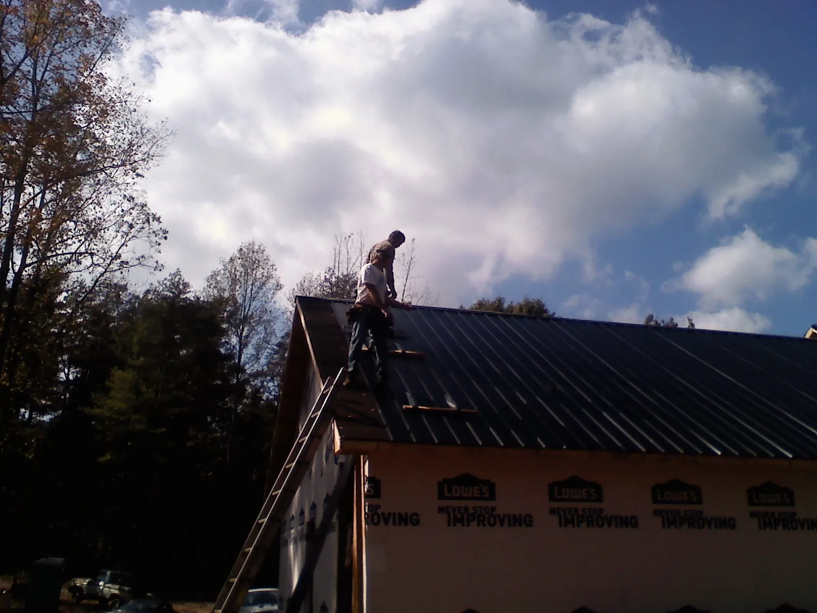 Roofer fastening dark metal panels high against a cloudy sky, from a Roof Inspection job in New Providence
