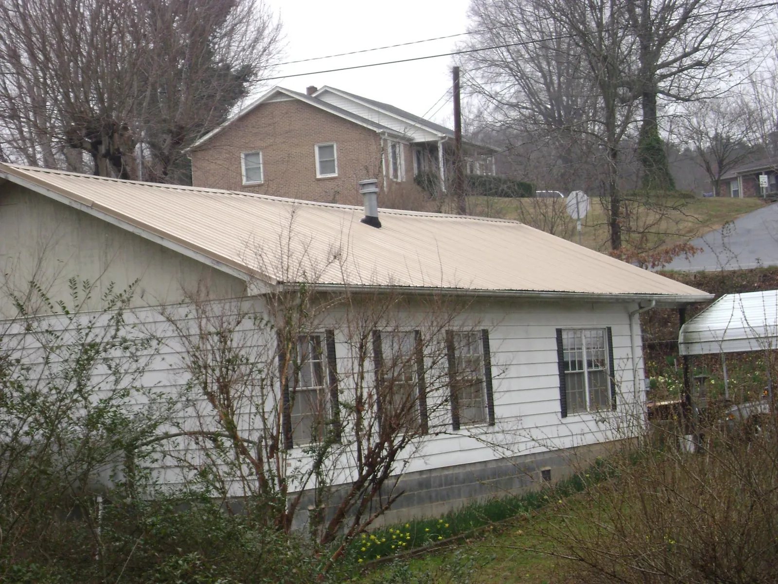 Tan metal roof on a white sided house set into a hillside — Commercial Roofing by Roofing Brothers in New Providence